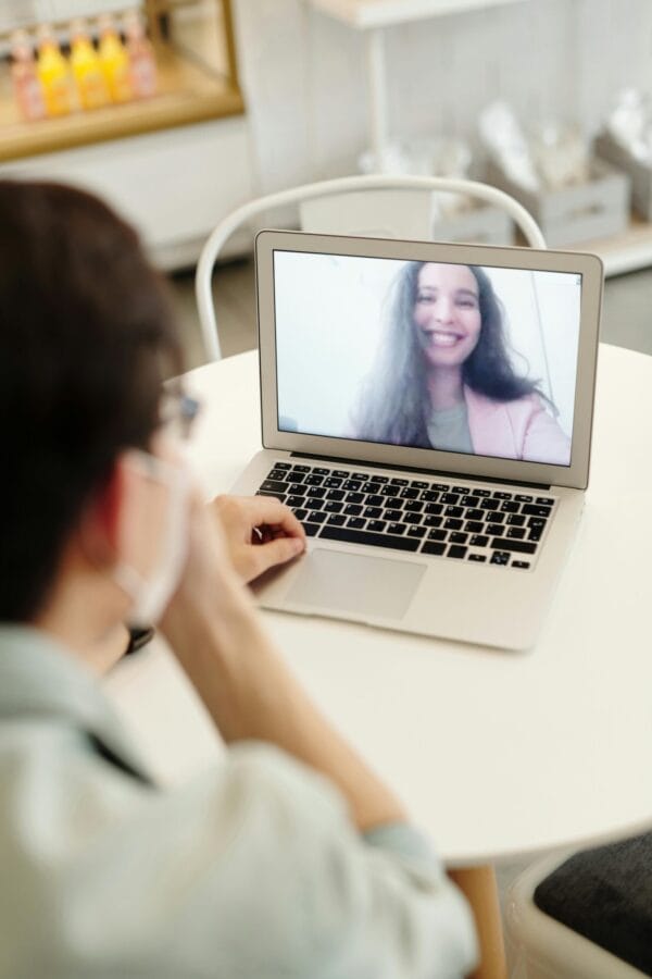 Primer plano de una videollamada que muestra a una mujer sonriente en la pantalla de un portátil en un acogedor entorno interior.