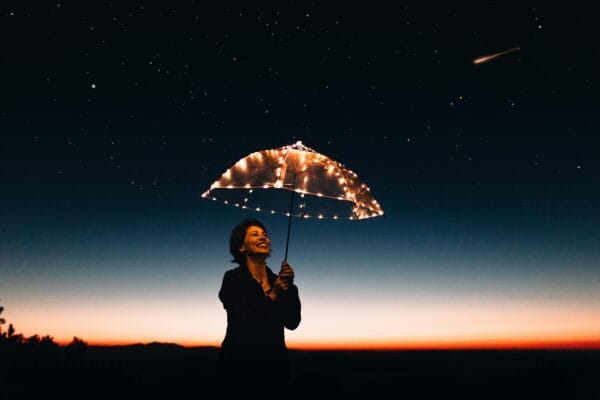 Una mujer alegre con un paraguas iluminado se encuentra bajo un cielo estrellado, capturando un momento mágico.